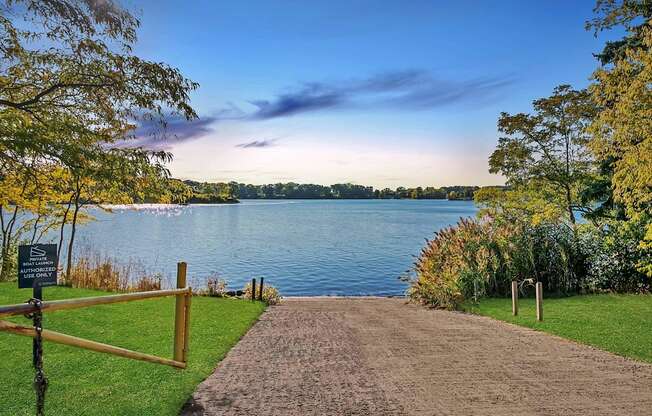 A pathway leads to a body of water with a sign on the left.