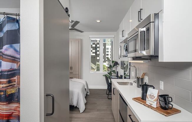 a kitchen with white cabinets and stainless steel appliances and a window with a view of a bedroom