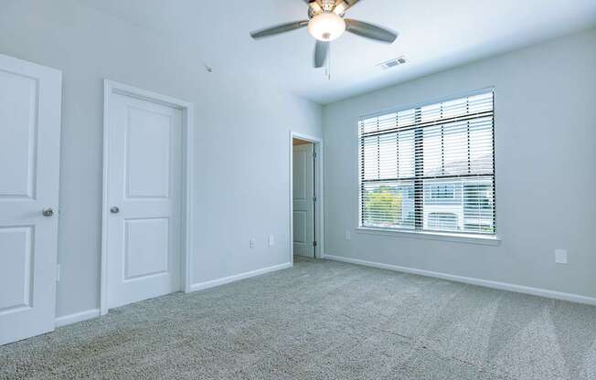 A room with a ceiling fan and a window with blinds.