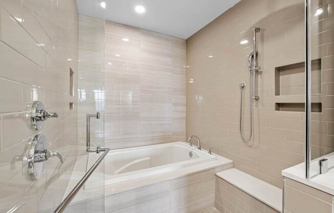 A modern bathroom with a walk-in glass shower and tub enclosure with tile walls at Alastair at Aria Village Apartments in Sandy Springs, GA