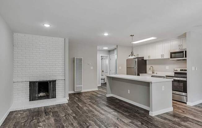 A modern kitchen with a white brick fireplace and wooden floors.