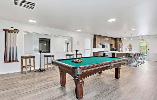 A pool table is in the middle of a room with a bar and a television.