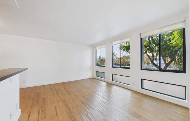 A room with wooden floors and white walls with three windows.