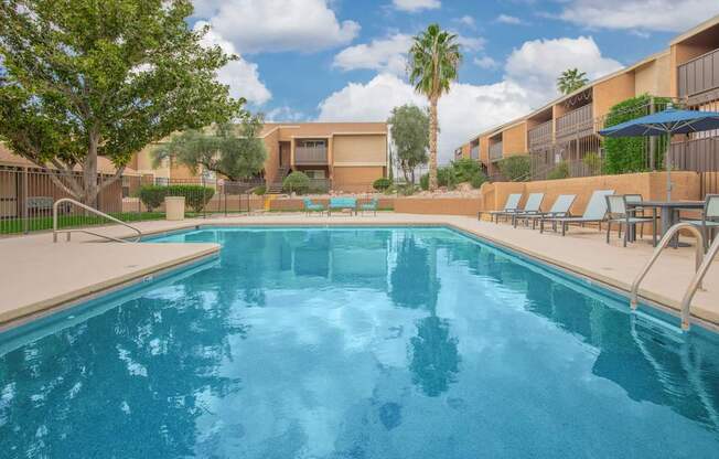 A swimming pool surrounded by lounge chairs and palm trees.