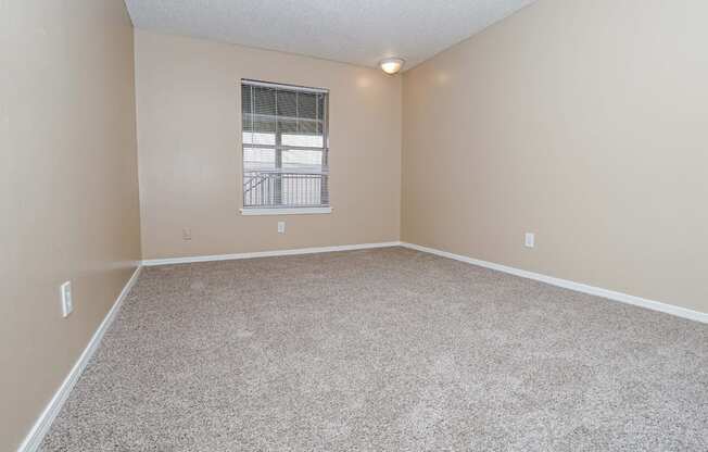 A bedroom with a carpeted floor and a window with blinds  at The Creole Apartments in Shreveport, LA