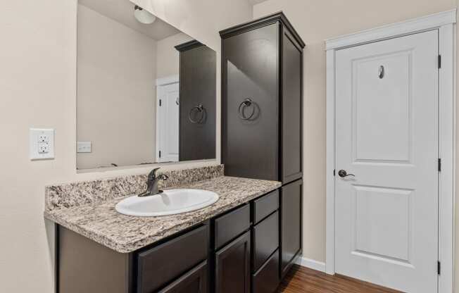 Little Tuscany Apartments & Townhomes - Apartment Bathroom with Dark Cabinets, Granite Countertops, Wood Plank Flooring, White Woodwork