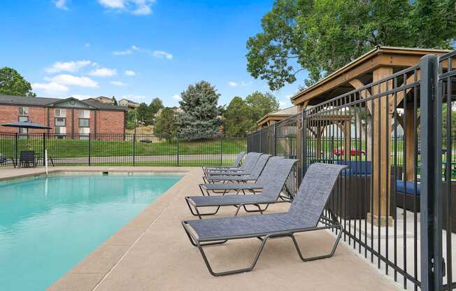 A pool with lounge chairs and a fence at Mountain Vista Apartments, Lakewood