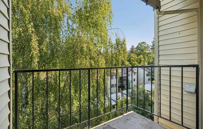 A balcony with a black railing overlooks a tree-filled street.