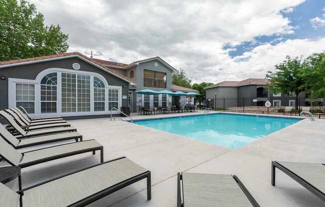 A pool area with sun loungers and a building in the background.