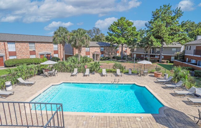 A fenced pool surrounded by lounge chairs and lush trees at Magnolia Apartments in Shreveport, LA