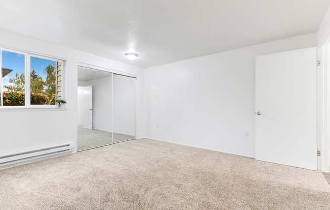 a spacious living room with white walls and carpeting and a large window