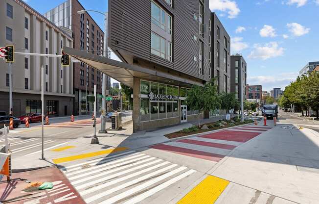 A crosswalk with red and white stripes is in front of a building with a glass facade.