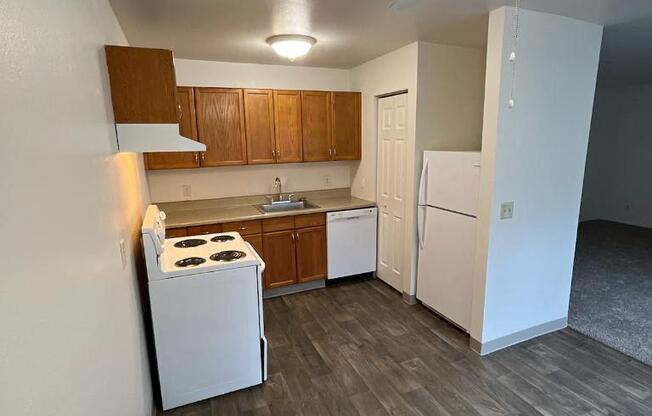 an empty kitchen with white appliances and wood floors