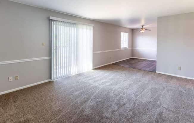 an empty living room with a large window and a ceiling fan
