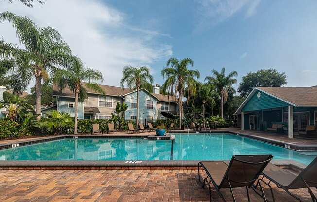 a swimming pool with chairs and palm trees in front of a house