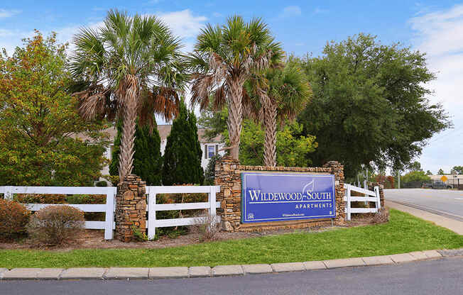 a sign in front of palm trees and a white fence