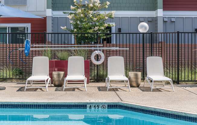 a swimming pool with three white chairs and a poolside umbrella
