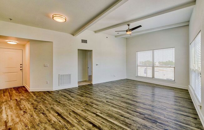 an empty living room with a large window and a ceiling fan