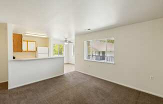 the living room and kitchen of an apartment with carpeting and a window