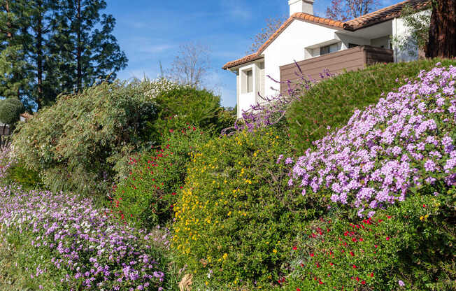 A white house with a brown roof is surrounded by a variety of colorful flowers.