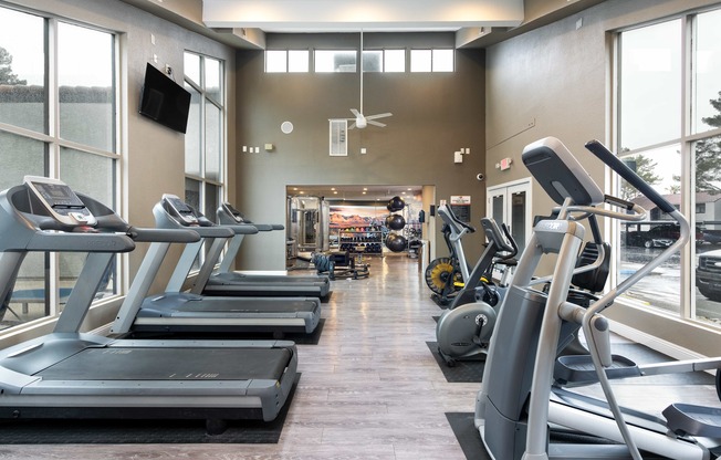 a gym with cardio equipment and large windows