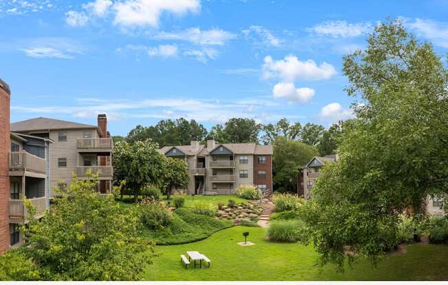 A grassy area with benches and trees in front of apartment buildings.