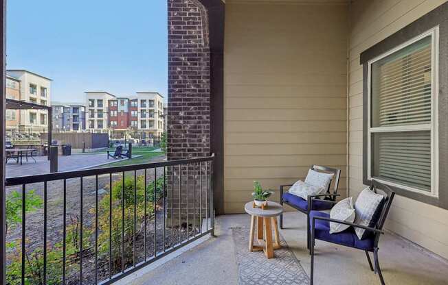 A balcony with a blue chair and a small table with a plant on it.