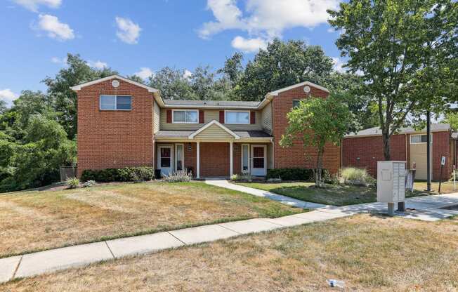 the front of a brick house with a lawn and trees