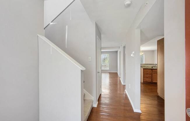 a hallway with white walls and a staircase with wood floors