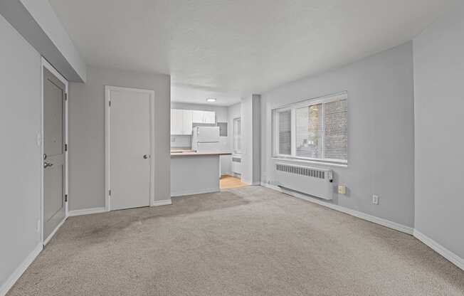 A spacious room with a carpeted floor and a window with blinds.