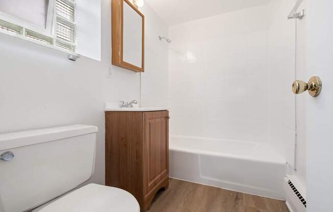 A white bathroom with a wooden cabinet and a white tub.
