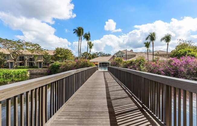 A wooden walkway leads to a row of houses with a blue sky and clouds in the background.