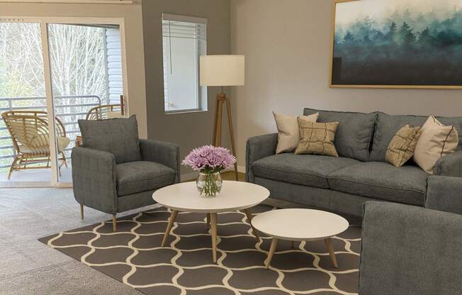 Living room with large sliding glass doors to private covered patio. Staged with 2 chairs, a couch, coffee tables, lamp.at Sitka Heights, Fife Washington