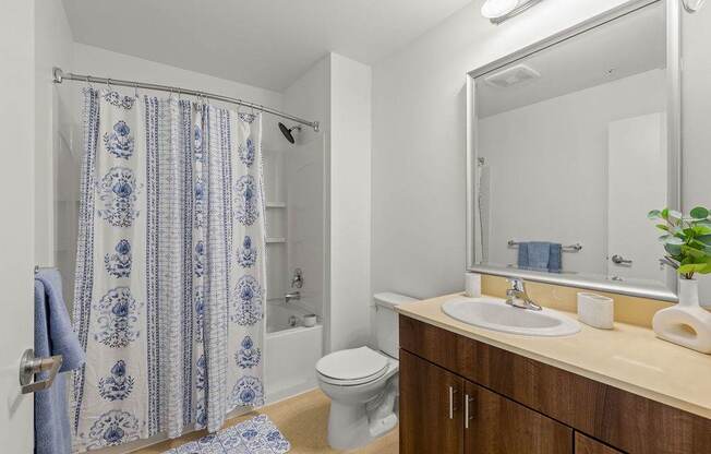A bathroom with a white toilet, a sink, a mirror, and a shower with a blue and white shower curtain.