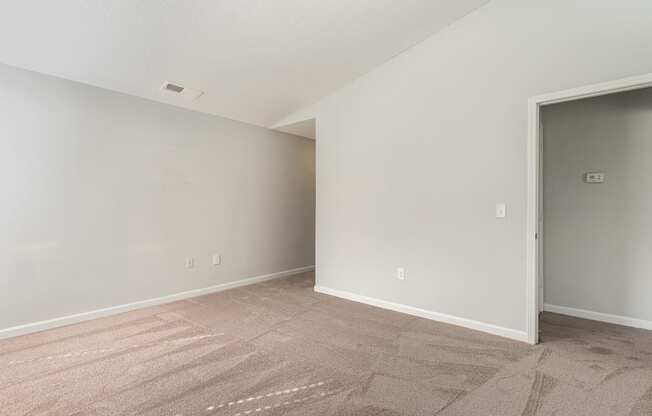 an empty living room with carpet and a door to a bedroom