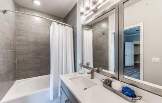 A modern bathroom with a white tub, sink, and grey tiled walls.