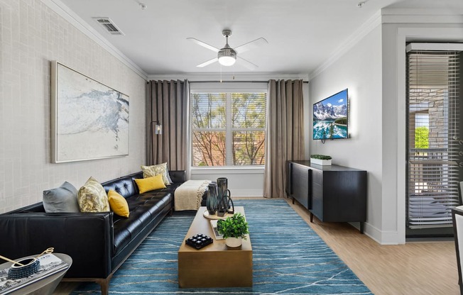 A living room with a black couch and a blue rug.