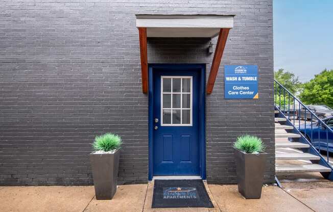 Blue door on the side of Stadium 700 Apartments in Arlington, TX next to a sign that reads "Wash & Tumble: Clothes Care Center"