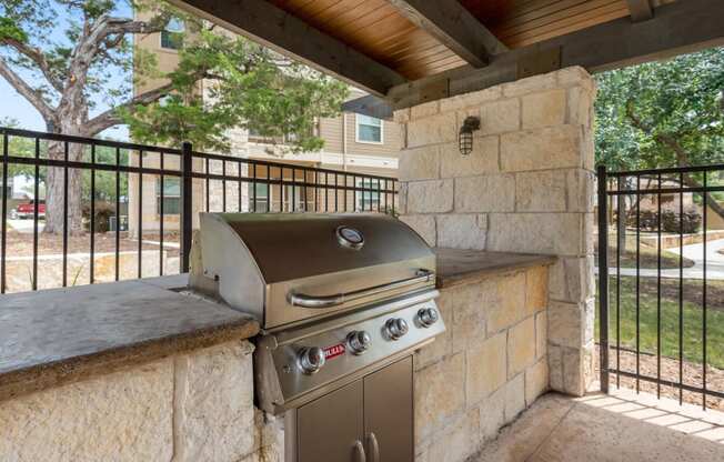 an outdoor kitchen with a grill and a bar with stone walls and a fence