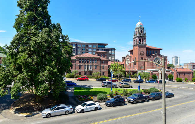 A church with a clock tower is in the background of a street with cars parked on the side.