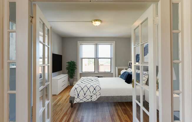 bedroom with bed, dresser, tv, hardwood flooring and large windows at the shawmut apartments in washington dc