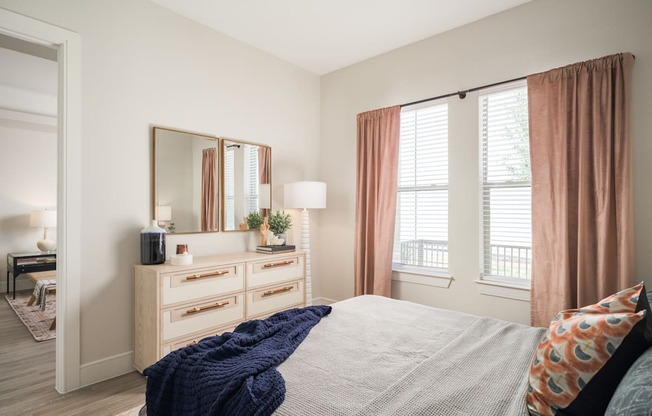 A bedroom with a bed, dresser, and window with curtains.