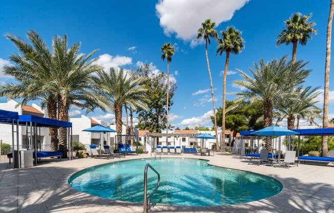 a swimming pool with blue umbrellas and palm trees in the background