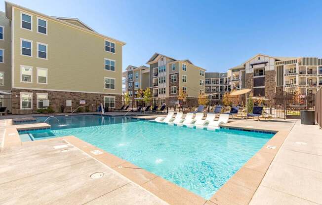 A swimming pool surrounded by lounge chairs and apartment buildings.