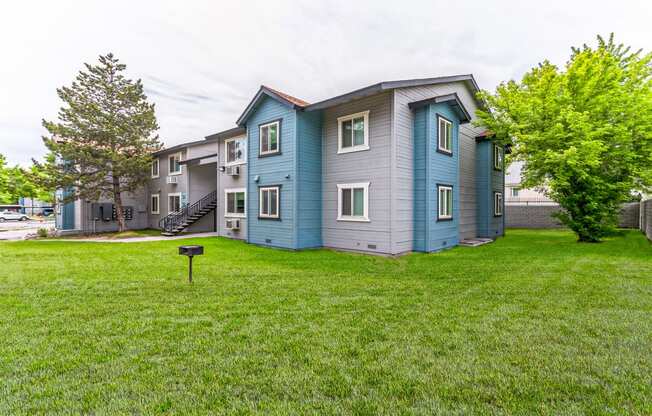 a blue and gray apartment building on a grassy lawn