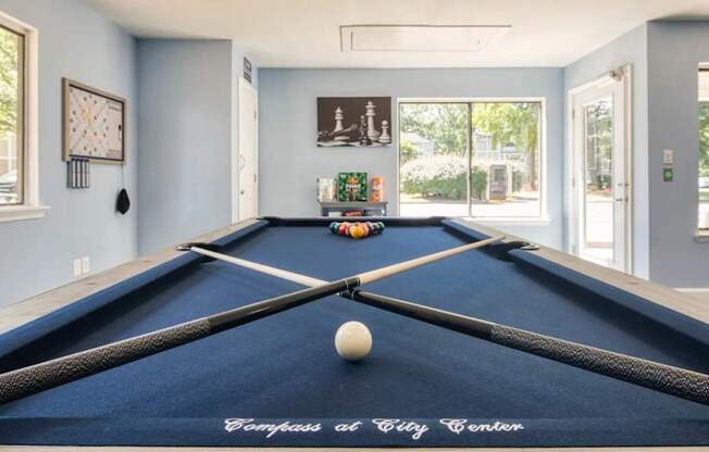 A pool table with a white ball and two cues in a room with a clock on the wall.