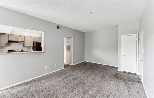 the living room and dining room of an apartment with white walls and carpet