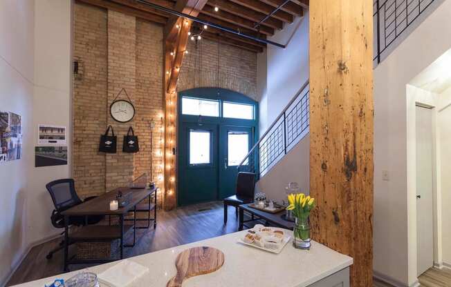 View of entryway from kitchen. Shows wood bean, exposed brick, and iron staircase.