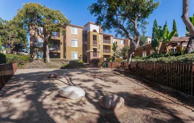 A sandy area with rocks and trees in front of apartment buildings.