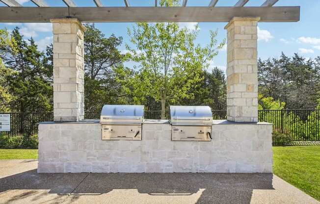 A stone structure with two grills under a wooden pergola.